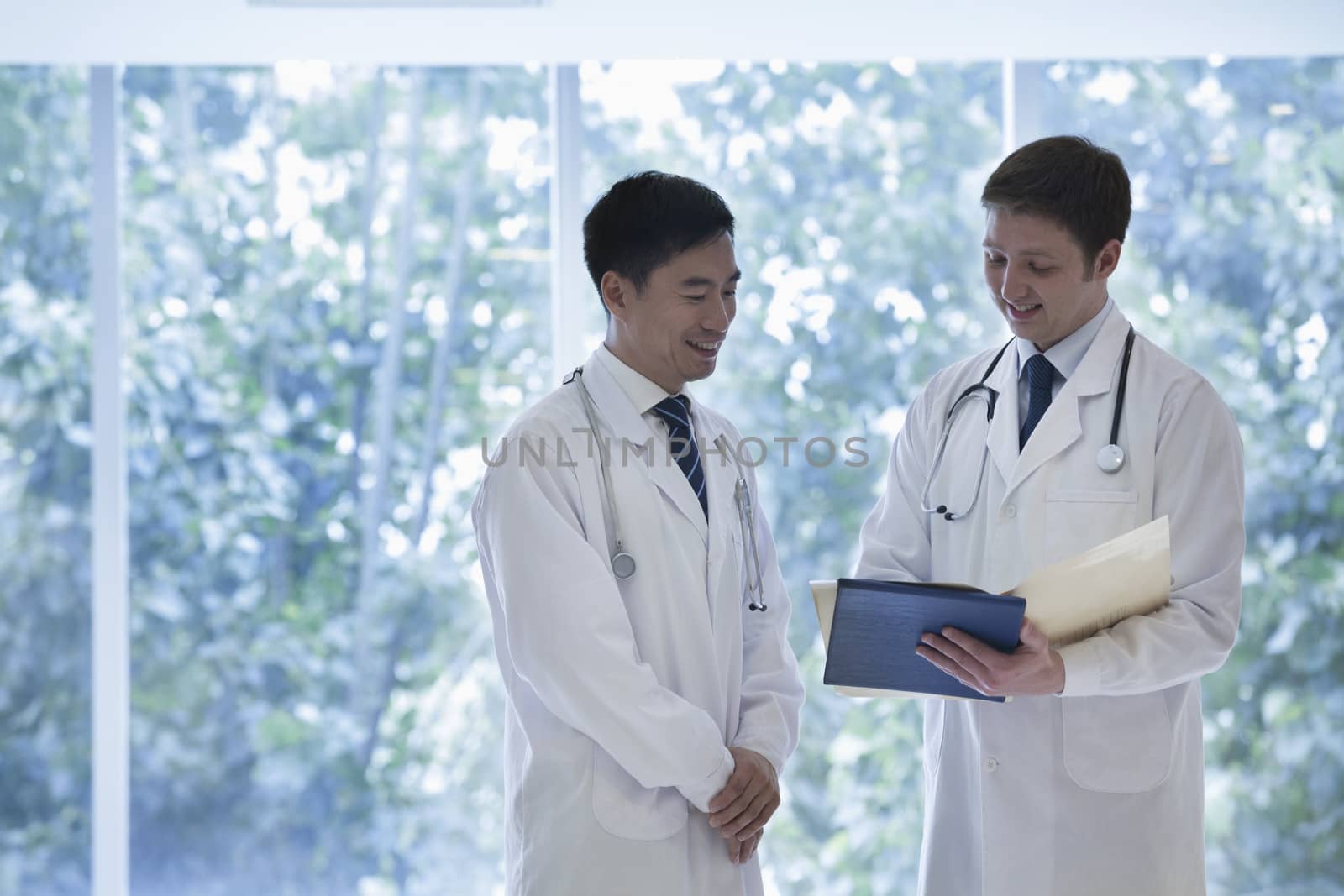 Two doctors standing, looking down, and consulting over medical record in the hospital by XiXinXing