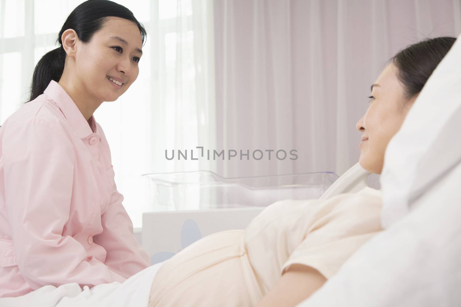 Smiling nurse talking to pregnant woman lying on bed in the hospital