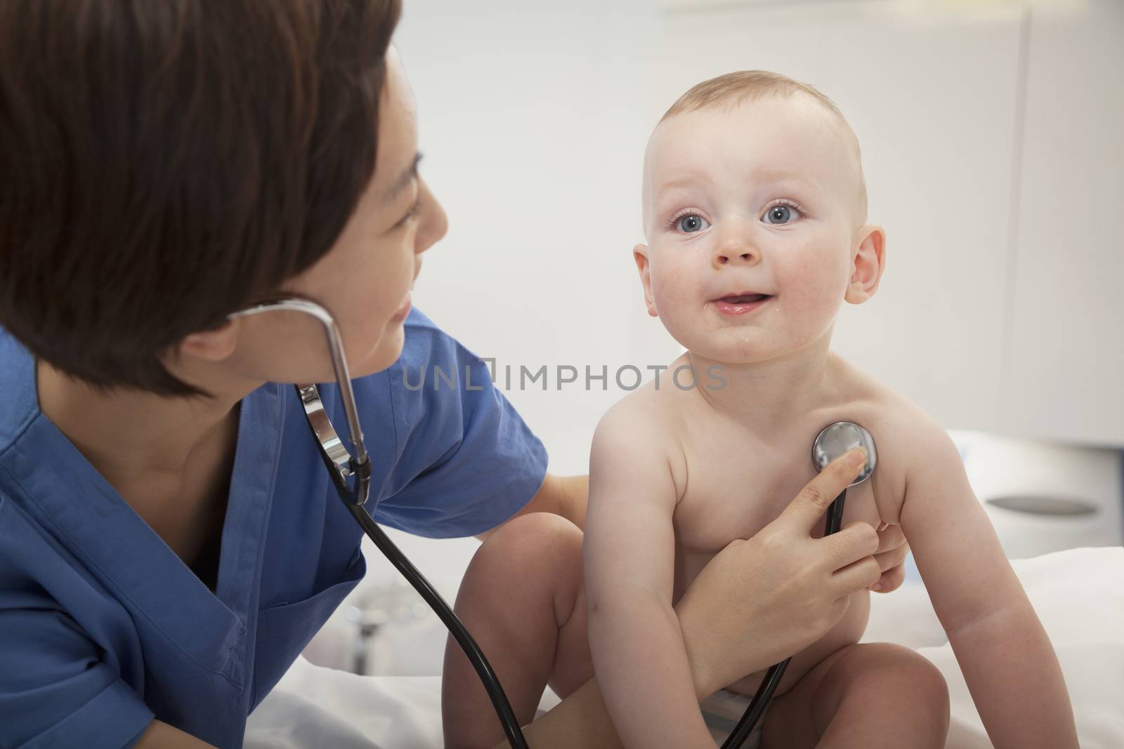 Smiling doctor checking a baby's heart beat with a stethoscope  in the doctors office
