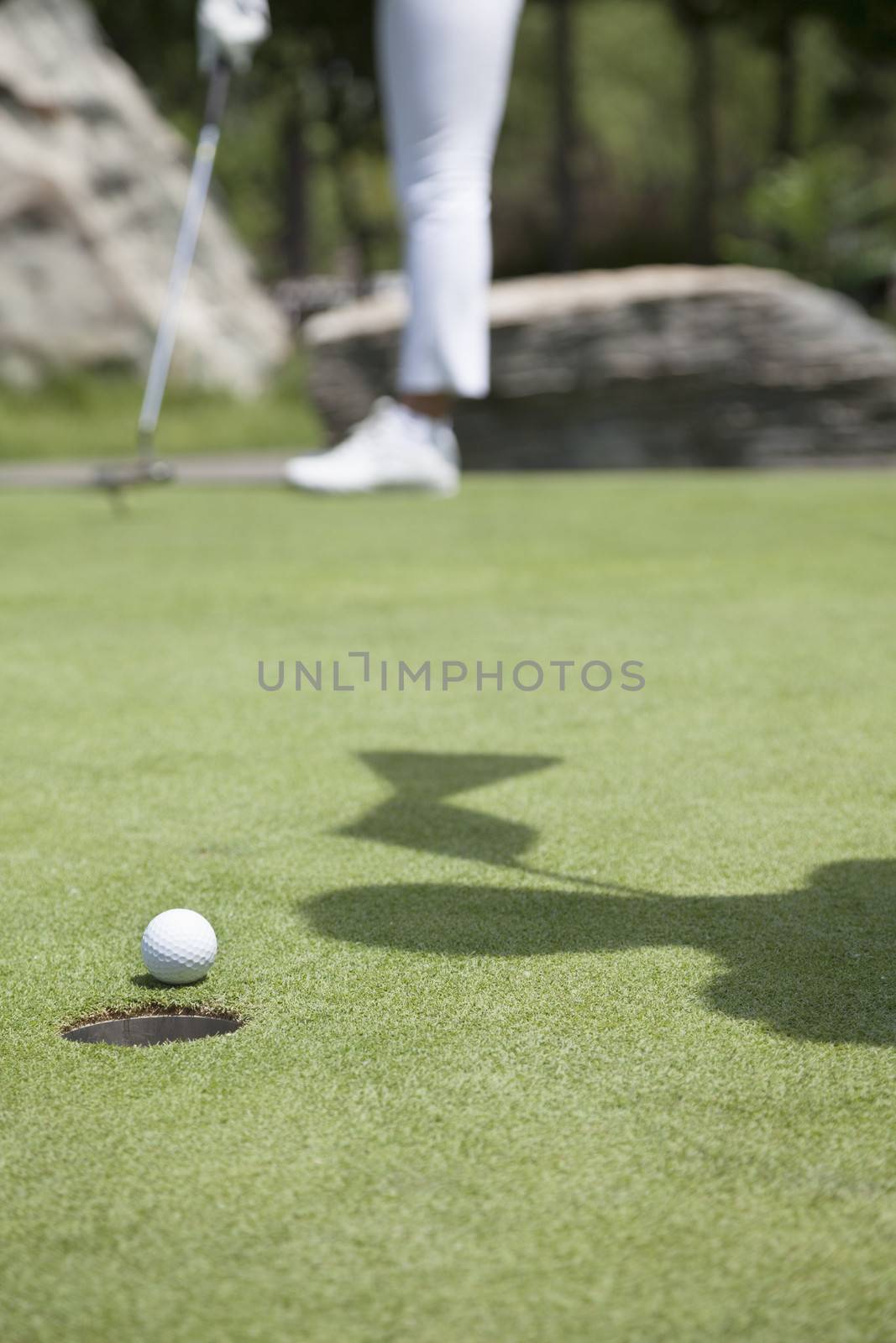 Low section of young woman hitting the ball on the golf course, focus on the hole