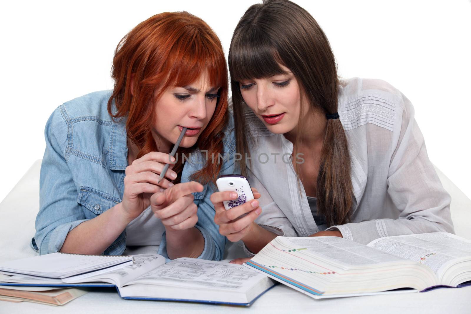 Girls looking at a cellphone while doing their homework by phovoir