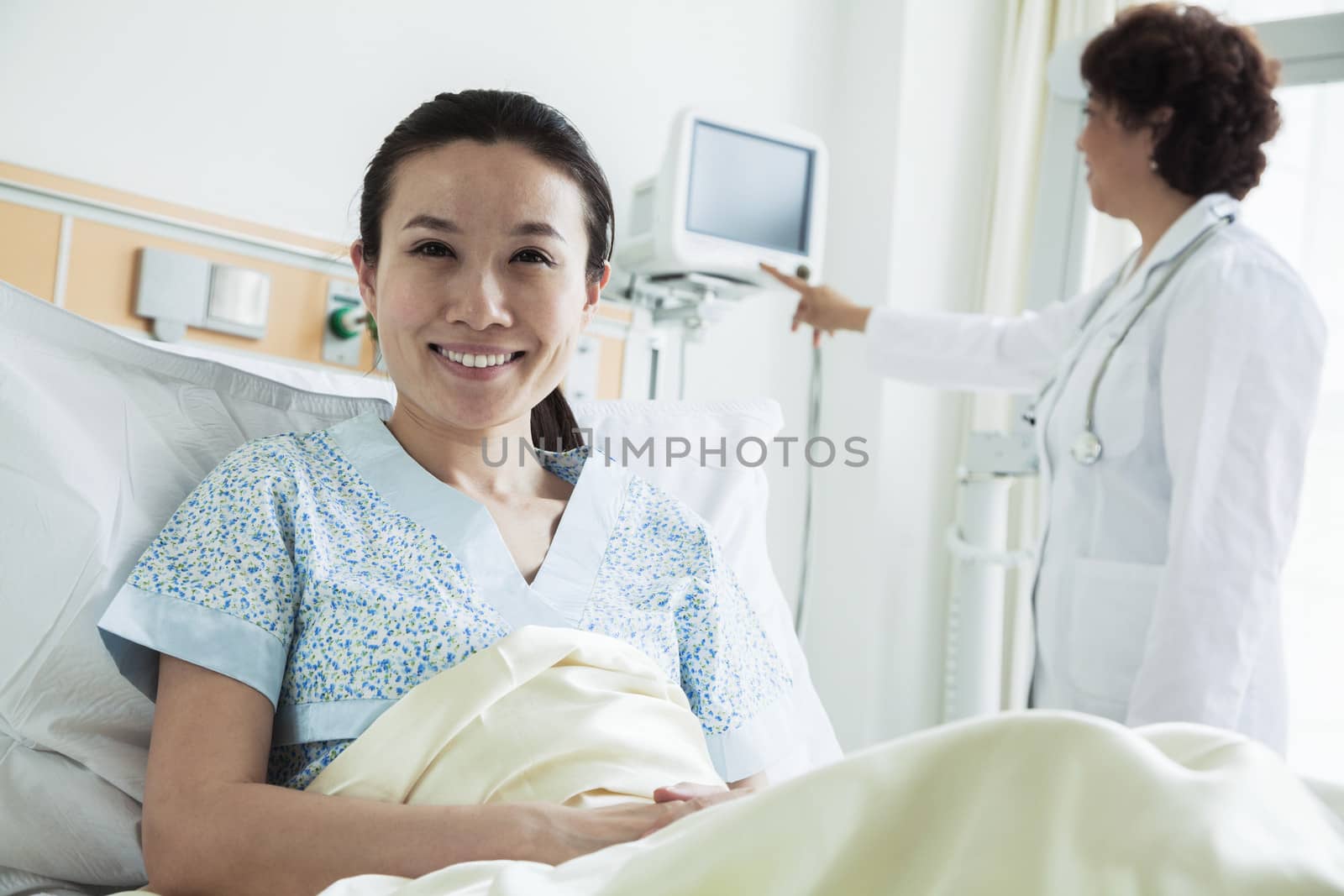 Smiling female patient sitting in a hospital bed, doctor using medical equipment in the background