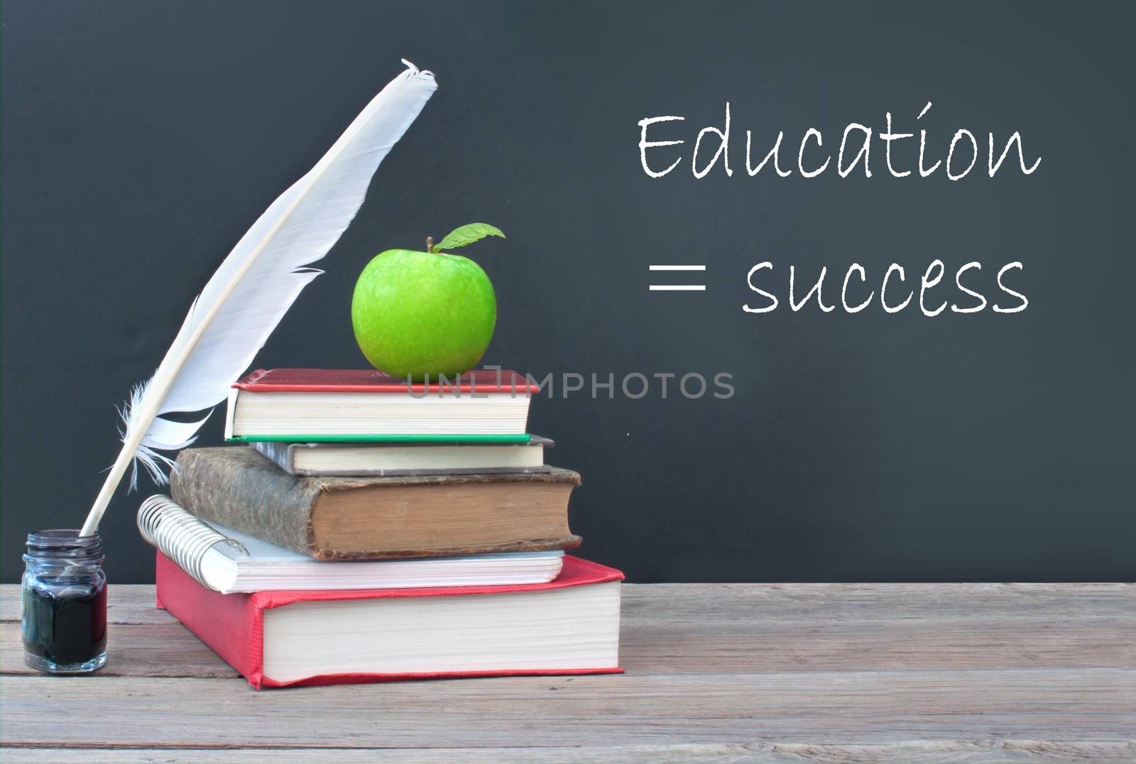 Education success written on a blackboard with a pile of books, quill and ink