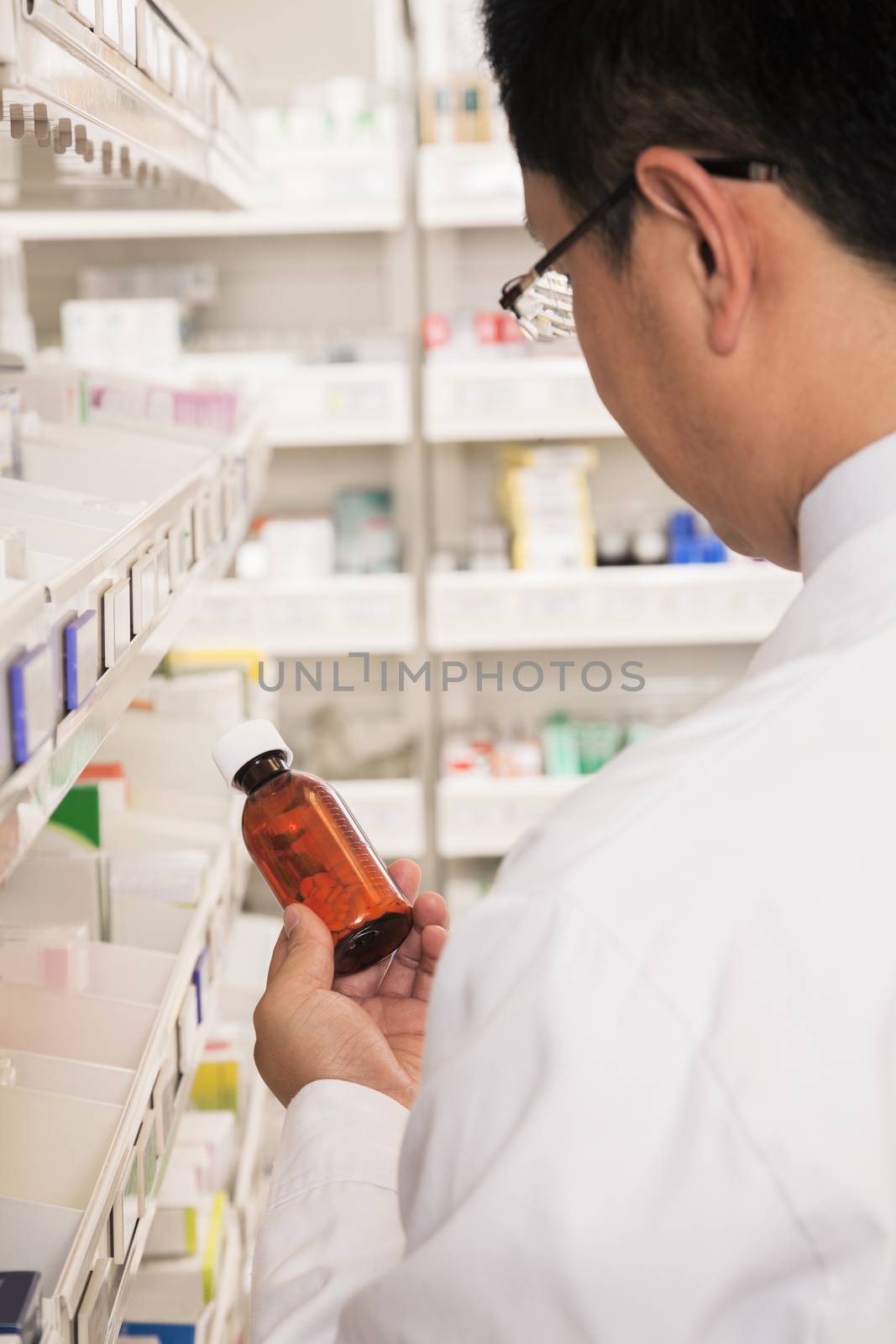 Pharmacist taking down and examining prescription medication in a pharmacy, rear view by XiXinXing