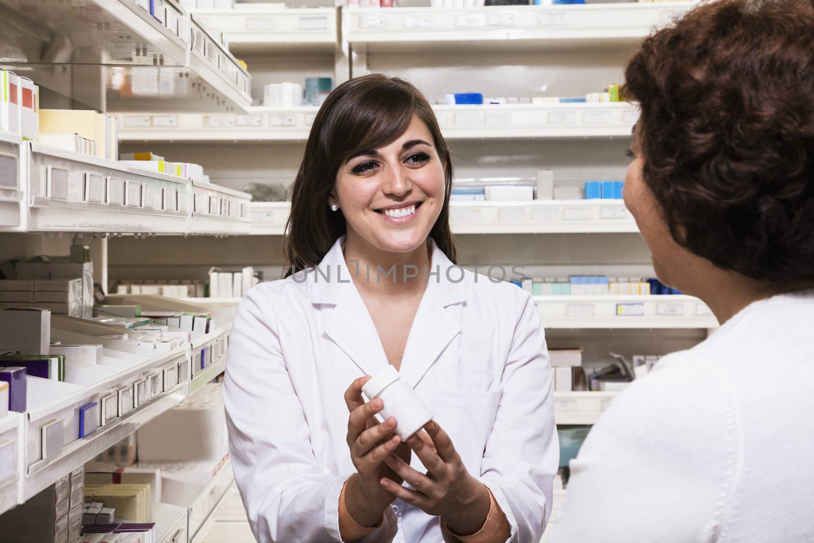 Smiling young pharmacist showing prescription medication to a customer by XiXinXing