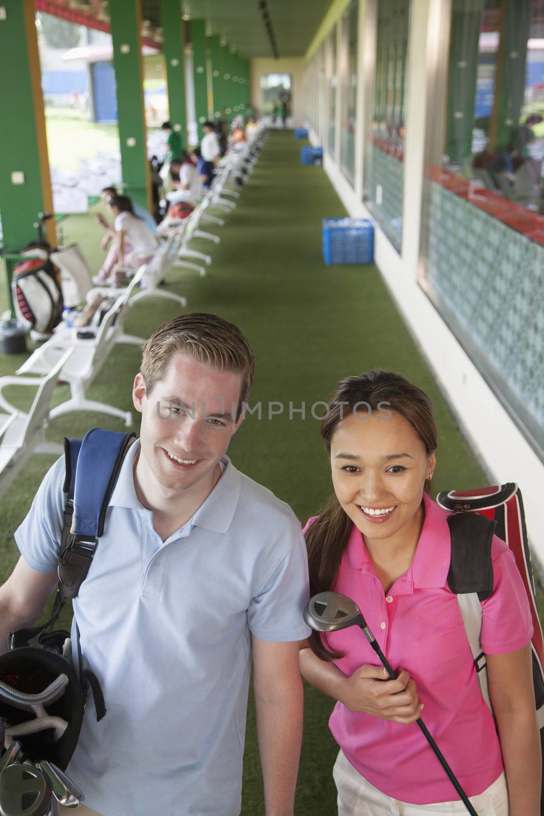 Young happy couple leaving the golf course with golf clubs and caddy