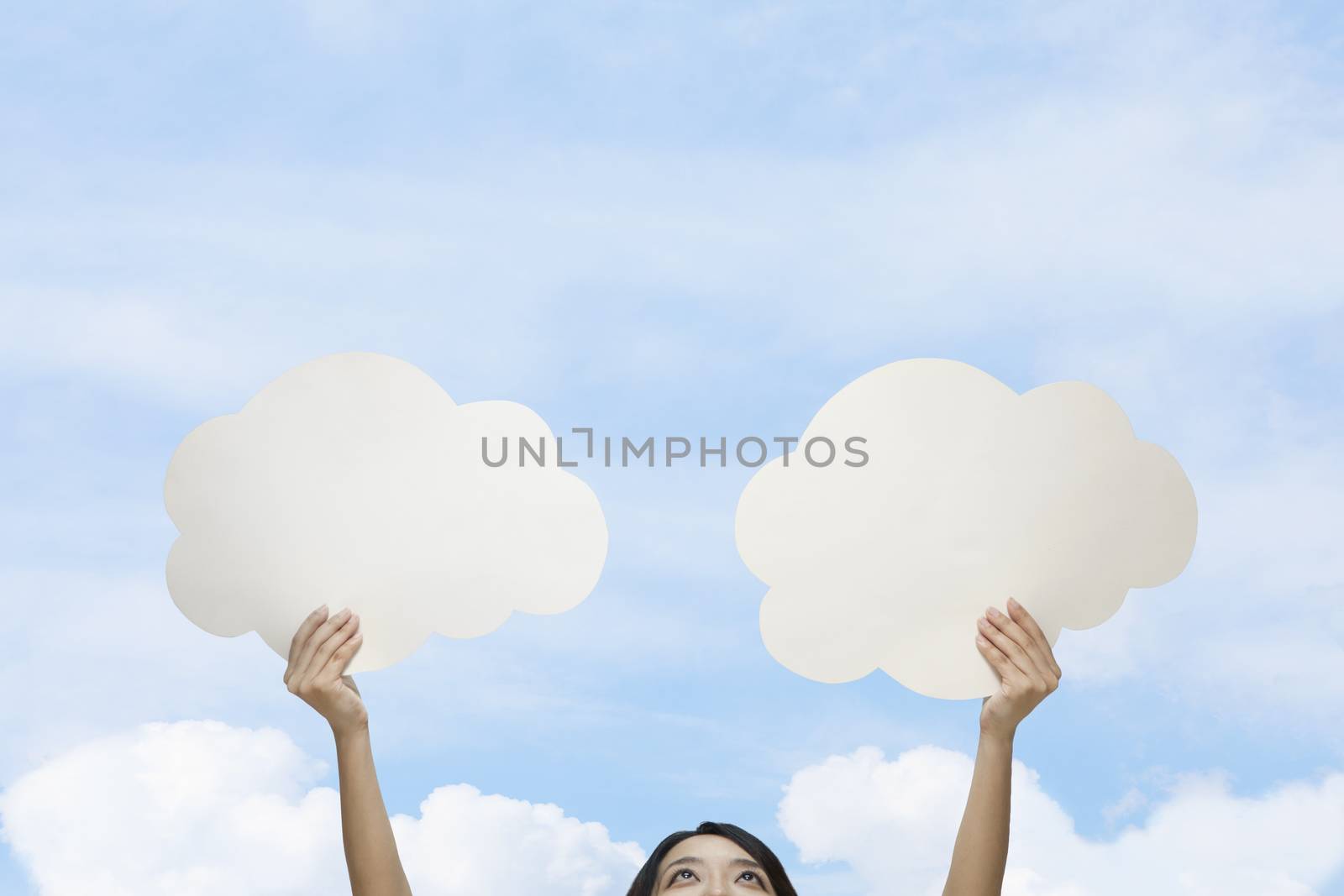 Young woman holding two cut out paper clouds against a blue sky with clouds