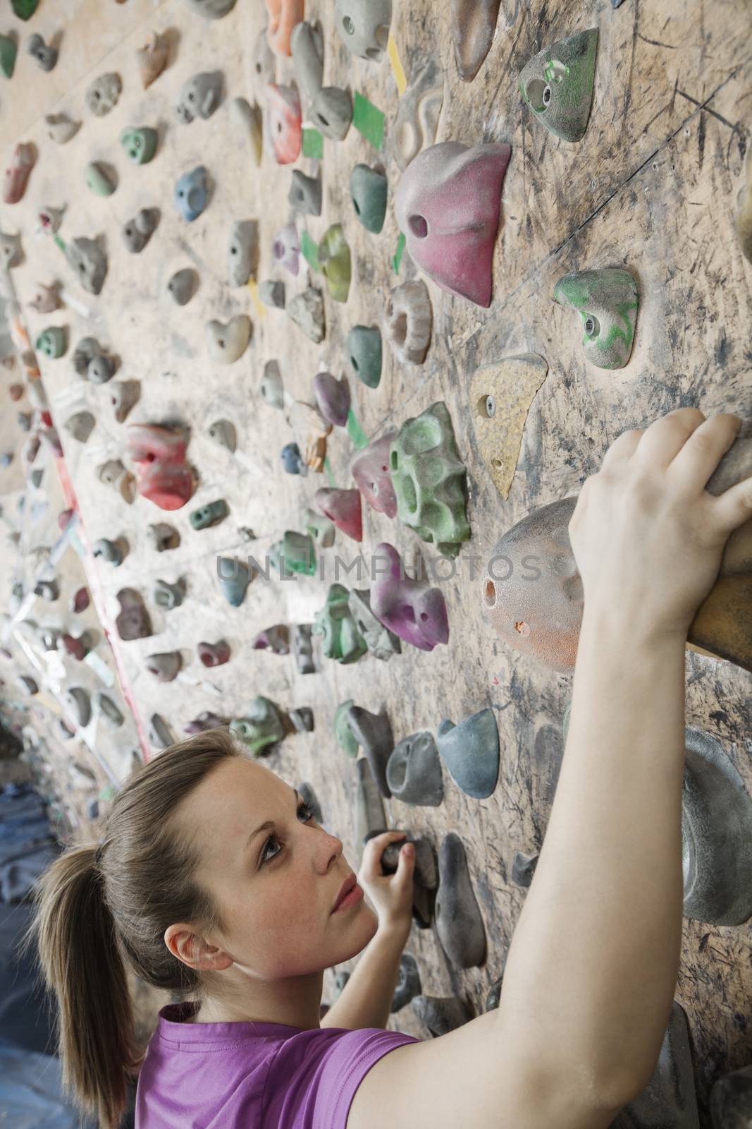 Determined young woman climbing up a climbing wall in an indoor climbing gym