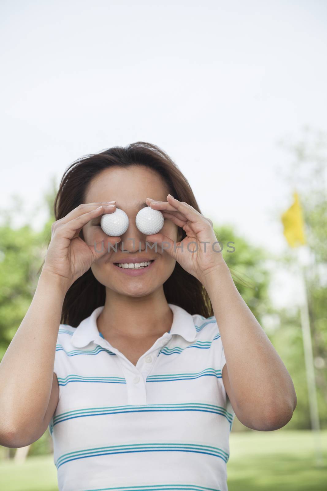 Smiling young woman holding up golf balls in front of her eyes