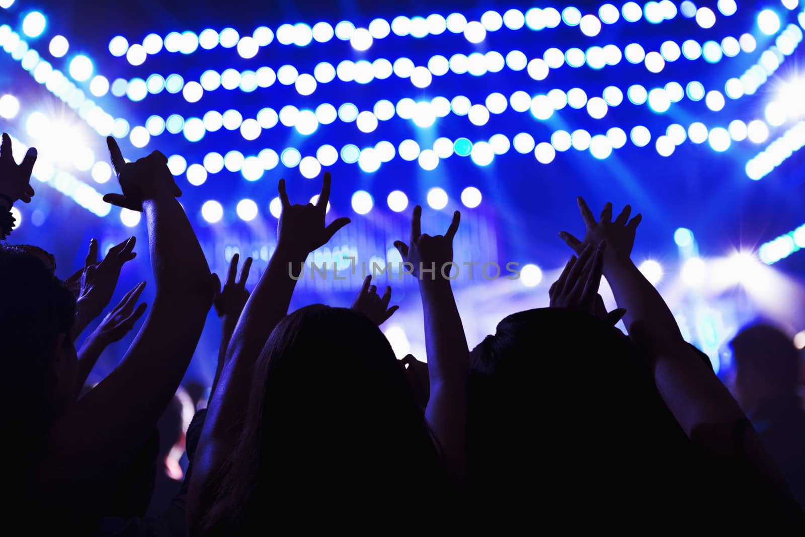 Audience watching a rock show, hands in the air, rear view, stage lights