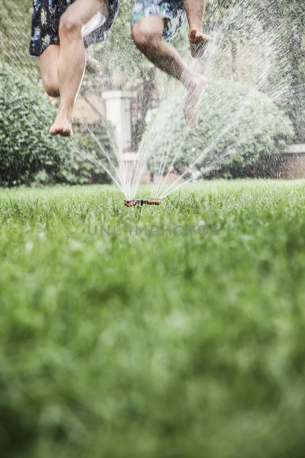 Two people jumping through a sprinkler, mid-air, surface level shot by XiXinXing