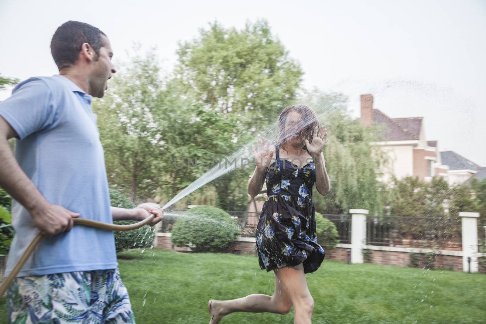 Couple playing with a garden hose and spraying each other outside in the garden 