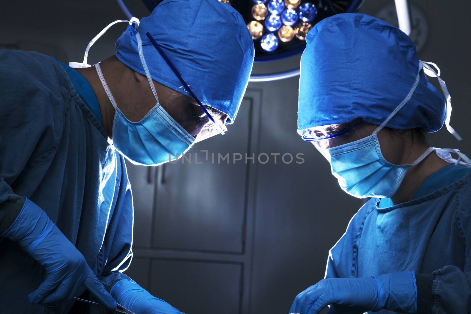 Two surgeons looking down, working, and concentrating at the operating table by XiXinXing