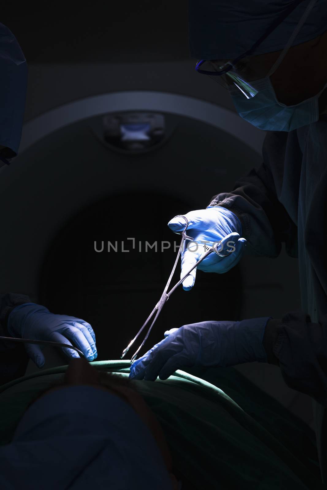 Surgeon looking down, working, and holding surgical equipment with patient lying on the operating table, dark