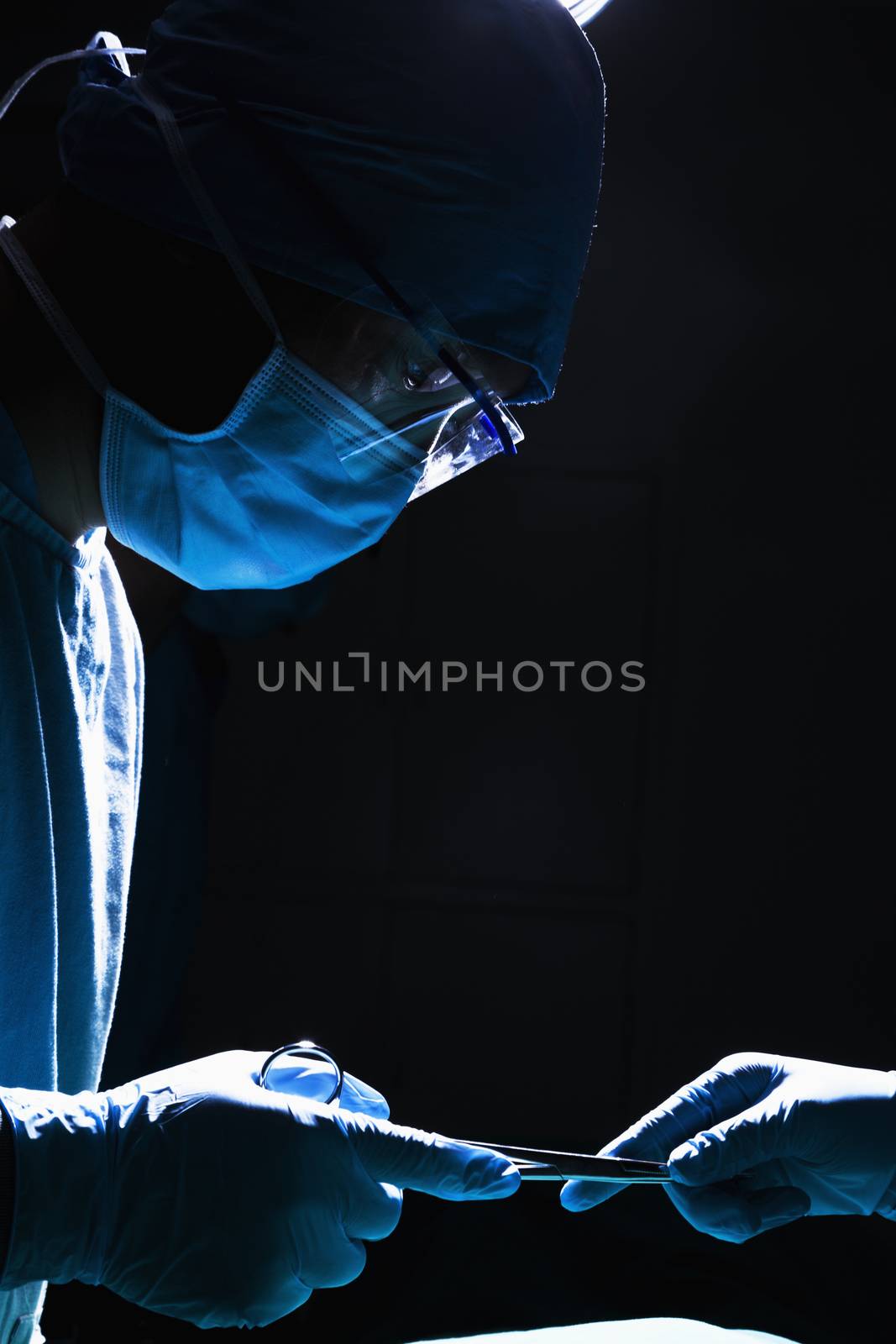 Two surgeons working and passing surgical equipment in the operating room, dark, close-up 