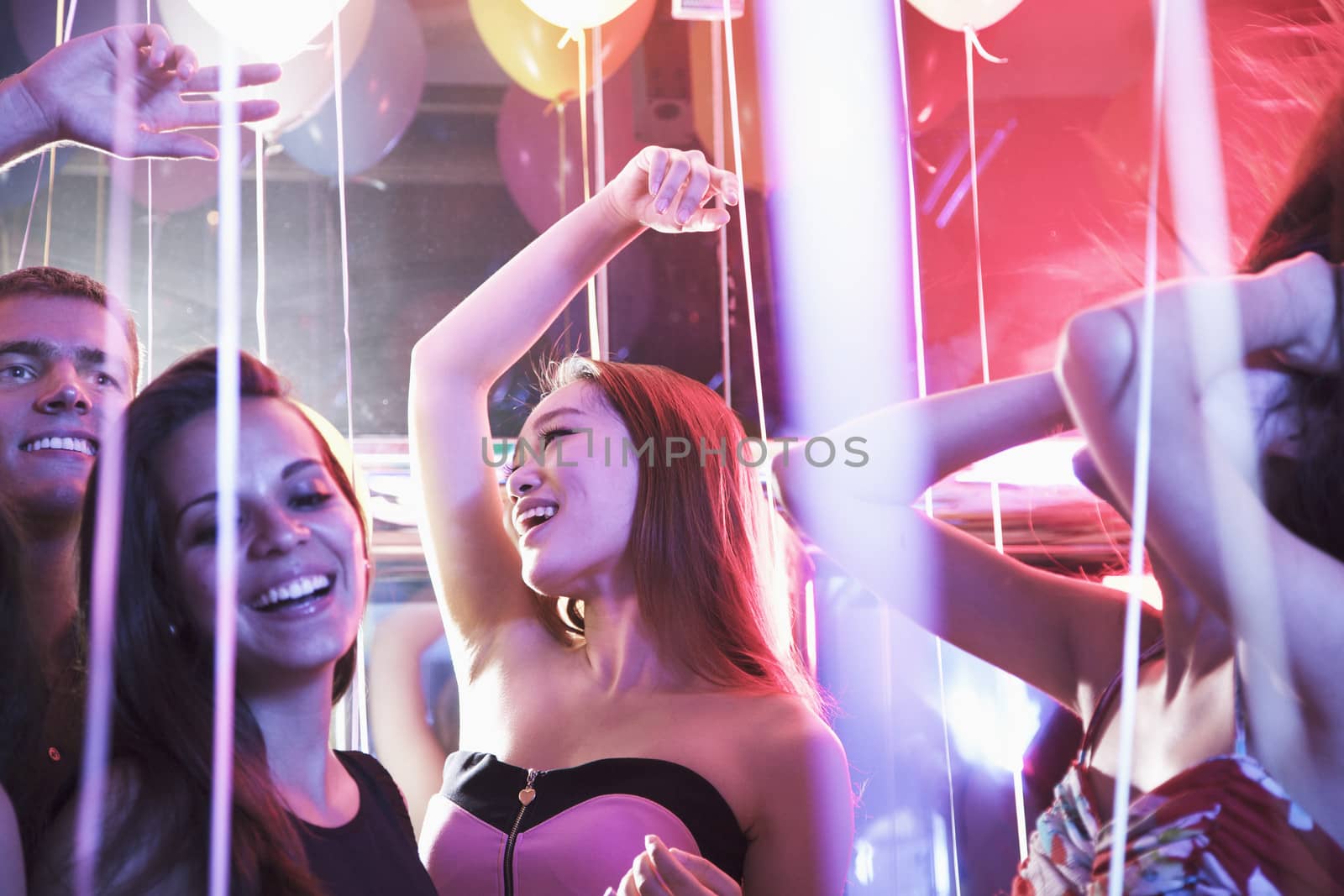 Multi-ethnic group of friends with hands in the air dancing among balloons in a nightclub