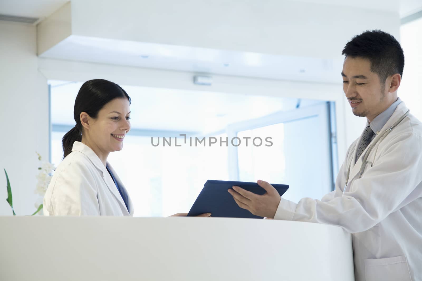 Two doctors standing by the counter and looking down at a document in the hospital