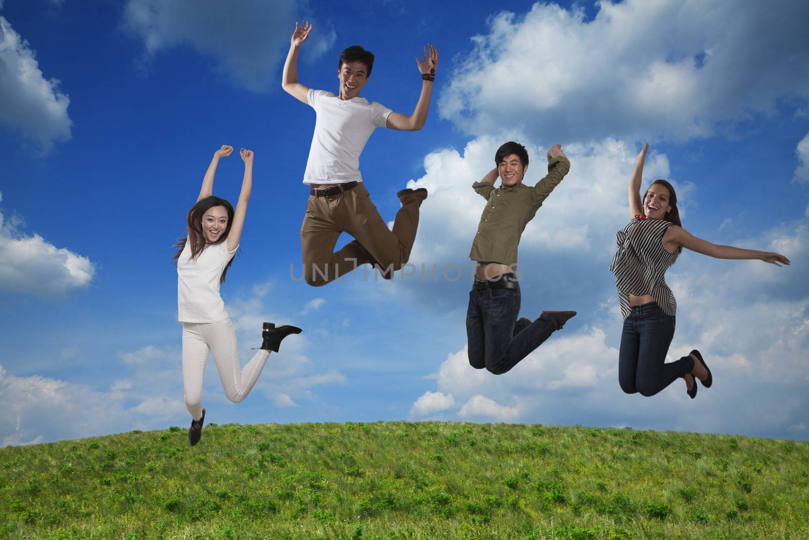 Four smiling friends jumping in mid-air, sky and cloud background