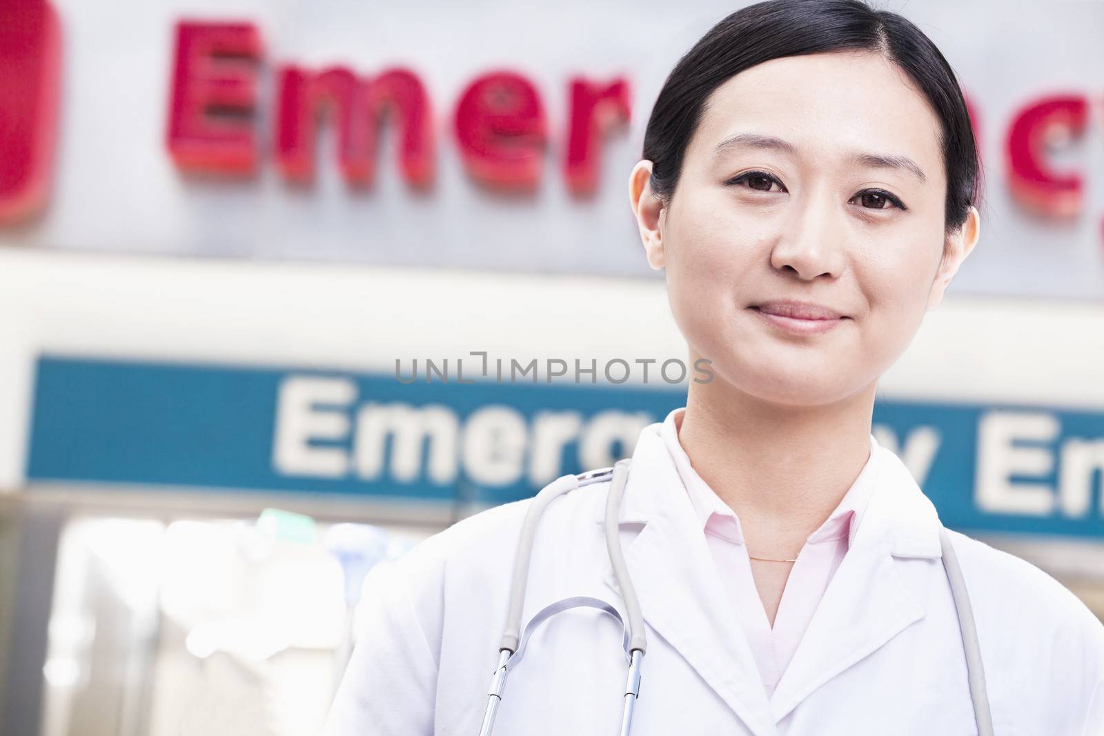 Portrait of smiling female doctor outside of the hospital, emergency room sign in the background