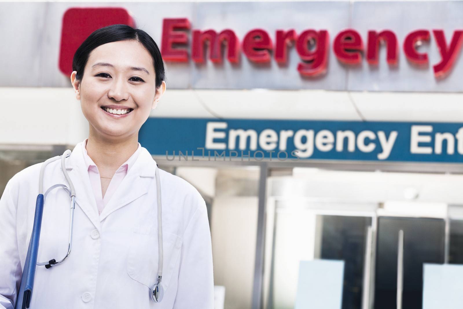Portrait of smiling female doctor outside of the hospital, emergency room sign in the background by XiXinXing