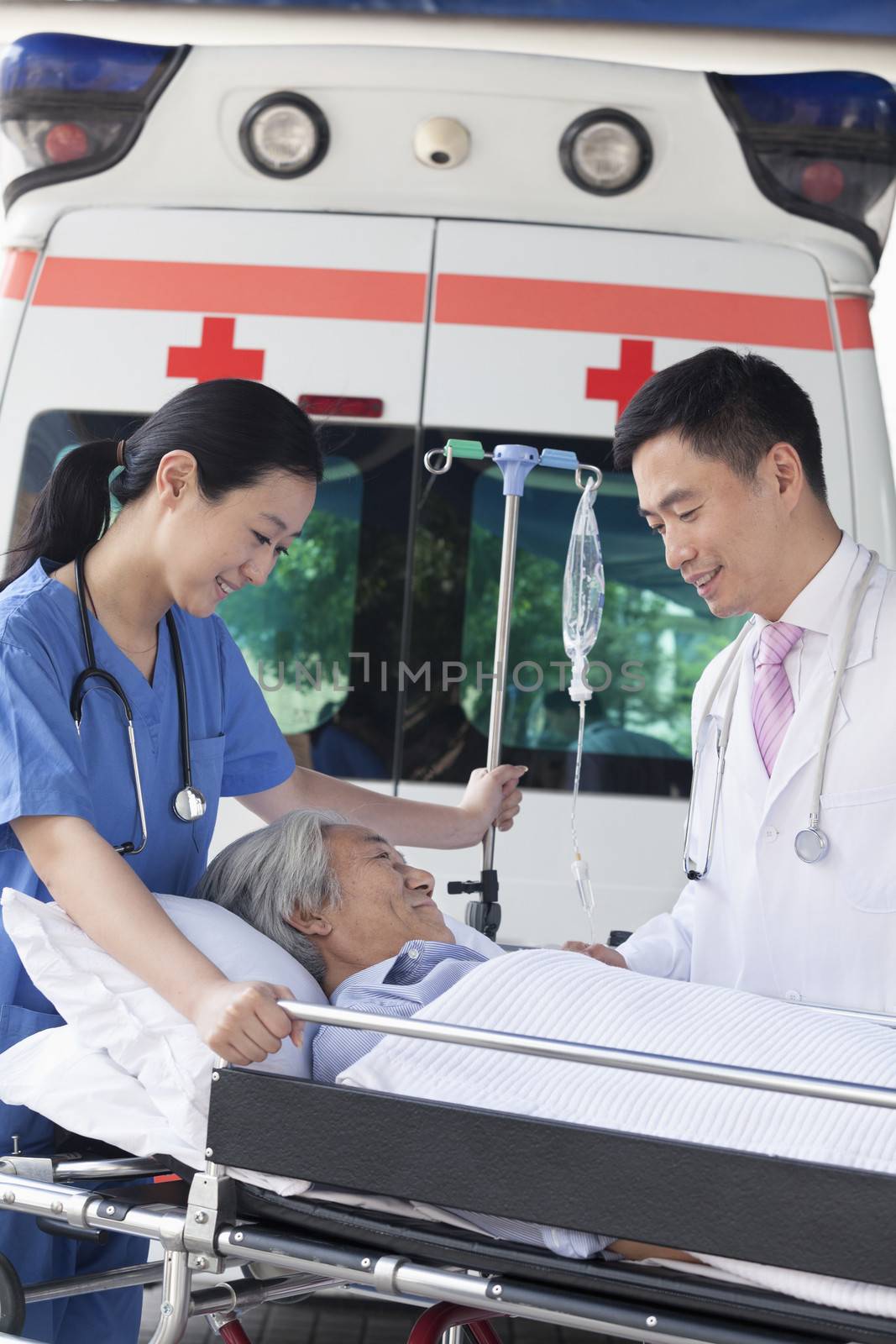 Female paramedic and doctor wheeling in a elderly patient on a stretcher in front of an ambulance