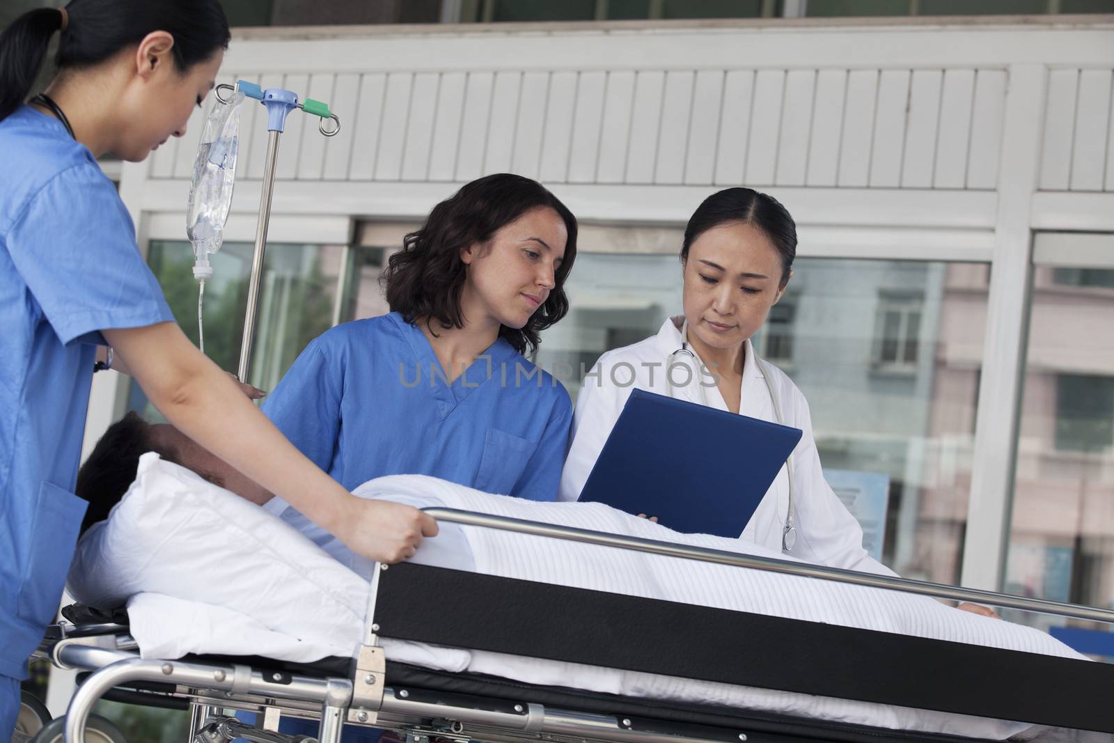 Paramedics and doctor looking down at the medical record of patient on a stretcher in front of the hospital