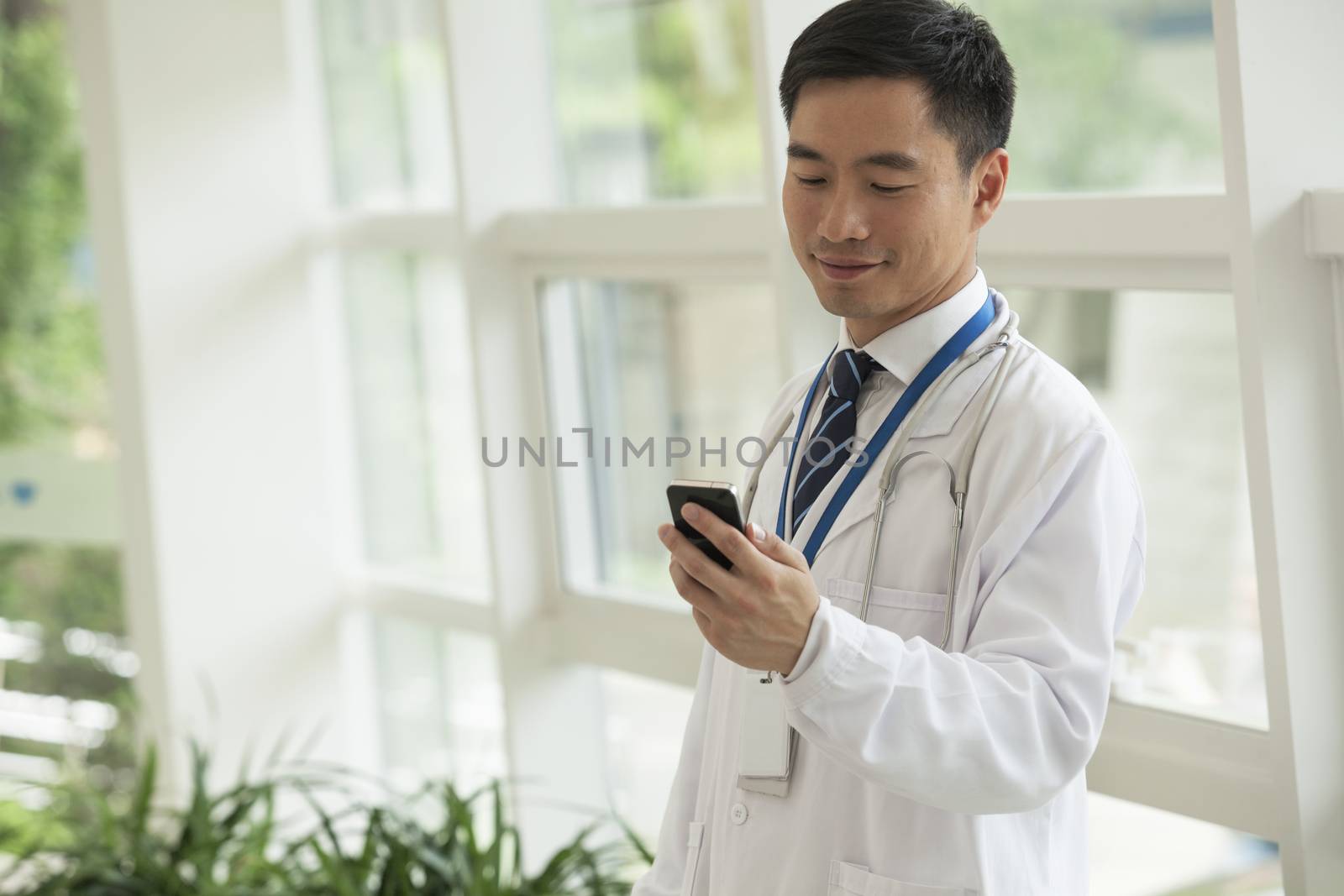 Smiling doctor looking down at his phone in the hospital lobby