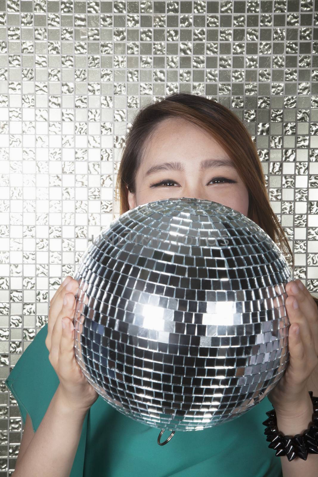 Young woman holding a disco ball, looking at camera in front of shiny wall