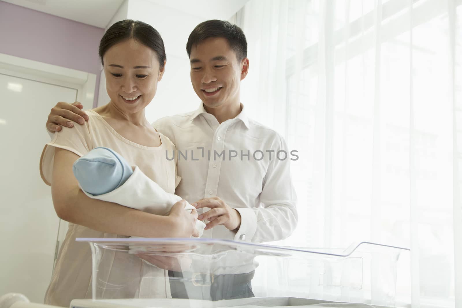 Young happy family holding their newborn in the hospital nursery