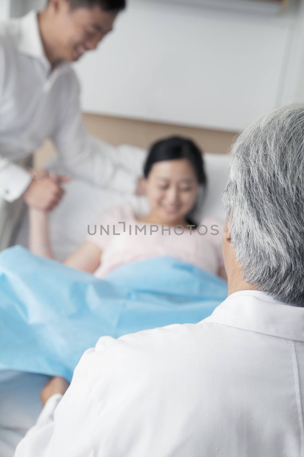 Women in labor holding her husbands hand with doctor in the foreground in the hospital by XiXinXing