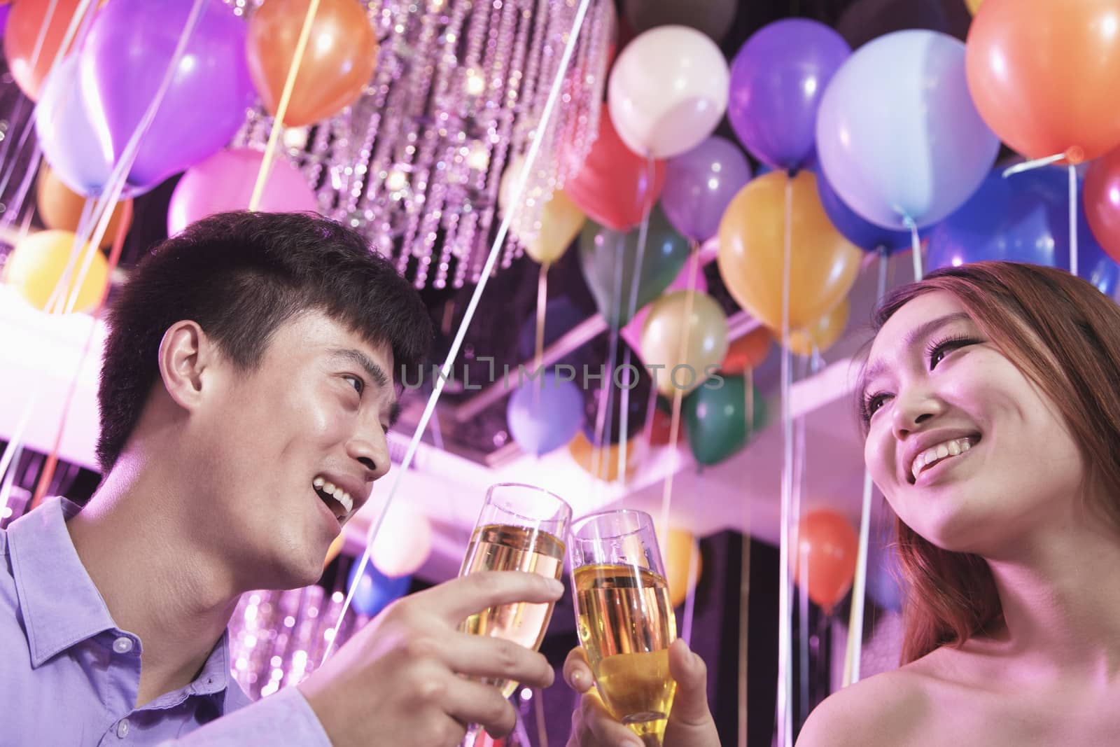 Two friends celebrating, toasting with champagne, nightclub in Beijing, balloons in the background