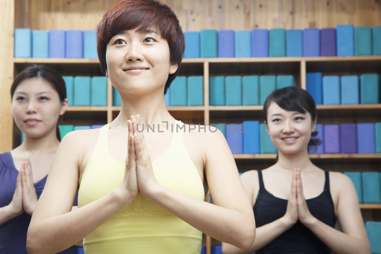 Three young women with hands clasped together in front doing yoga by XiXinXing