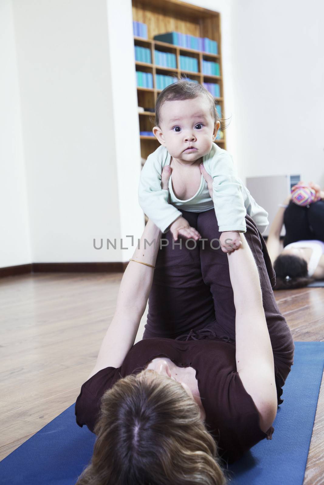 Mother lying on back and holding her baby during a yoga class by XiXinXing