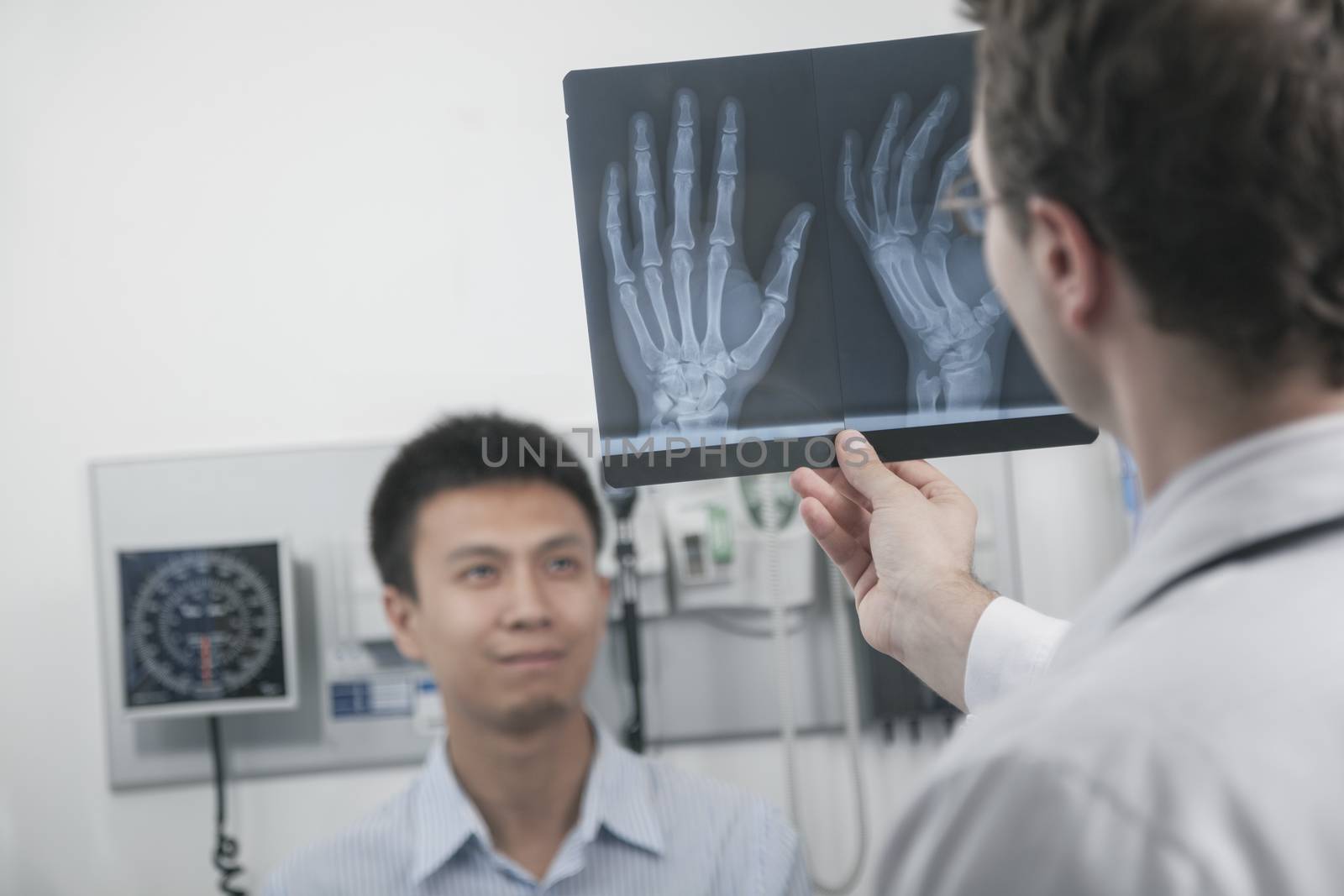 Doctor holding up and looking at x-ray of patients hand bones, patient in the background