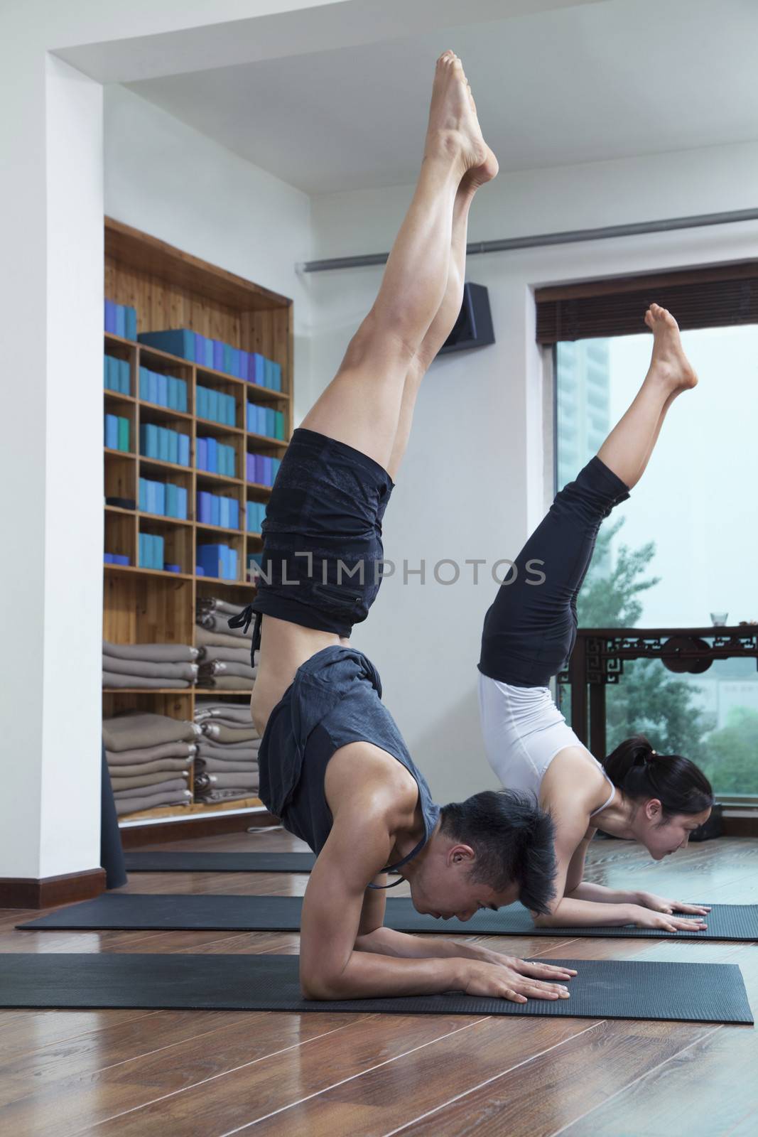 Two people with legs raised doing yoga in a yoga studio by XiXinXing