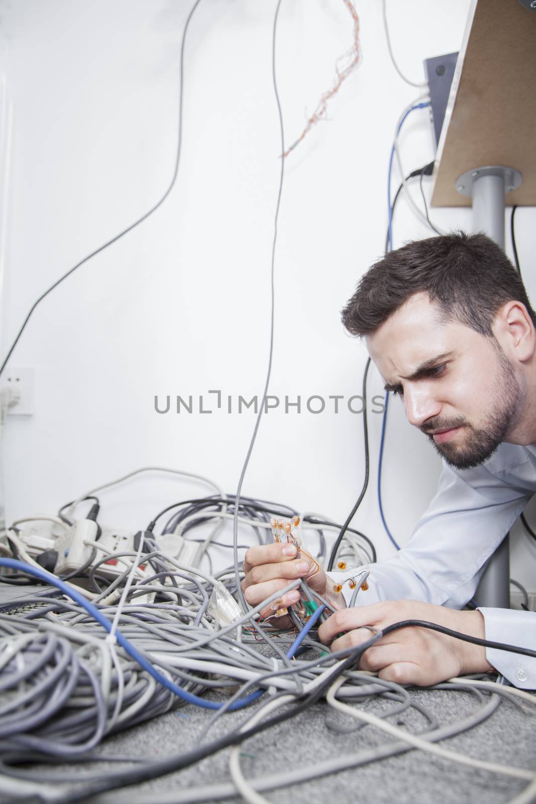 Frustrated man lying down trying to figure out and sort  computer cables