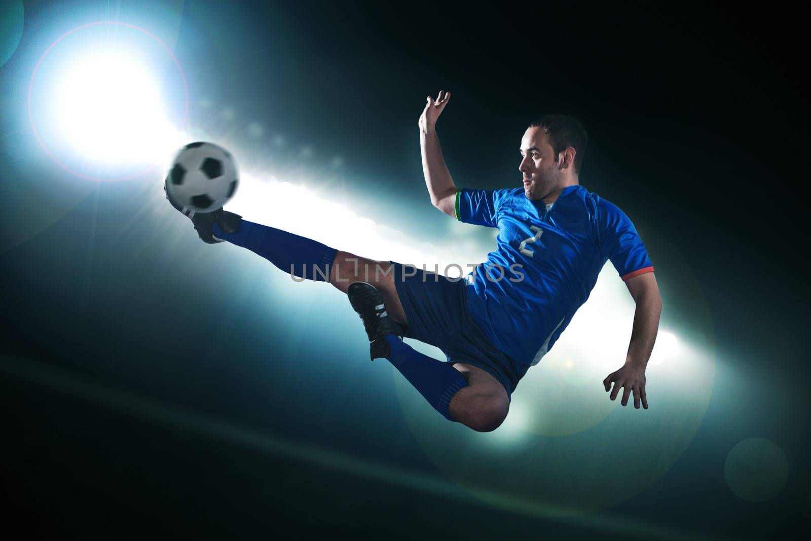 Soccer player in mid air kicking the soccer ball, stadium lights at night in background