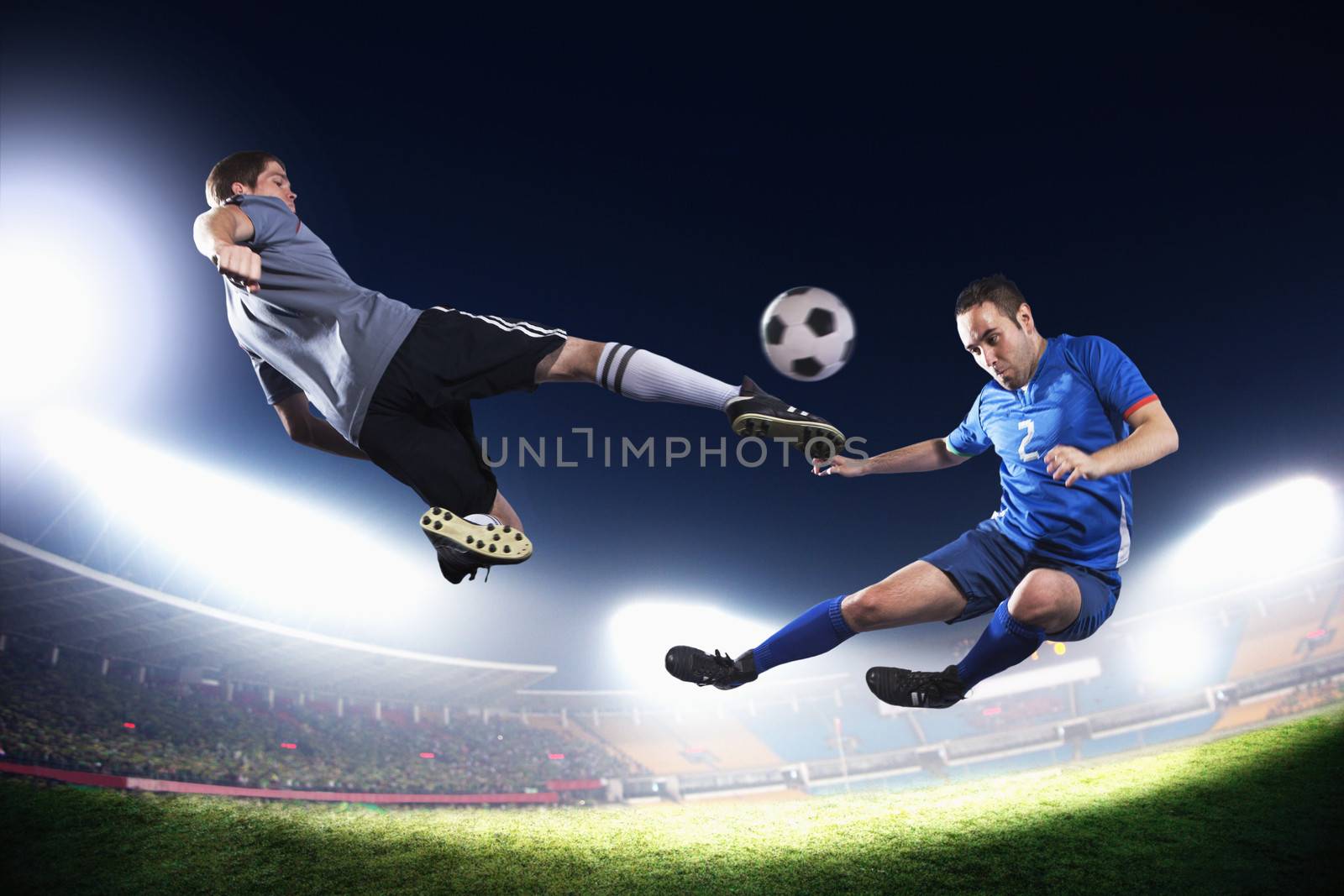 Two soccer players in mid air kicking the soccer ball, stadium lights at night in background