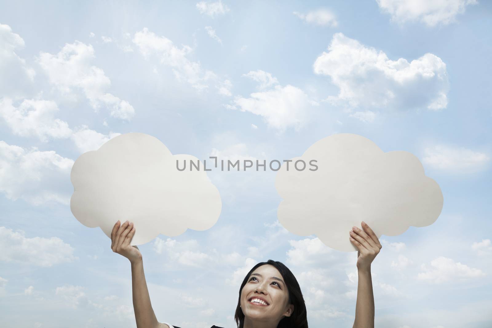 Young woman holding two cut out paper clouds against a blue sky with clouds