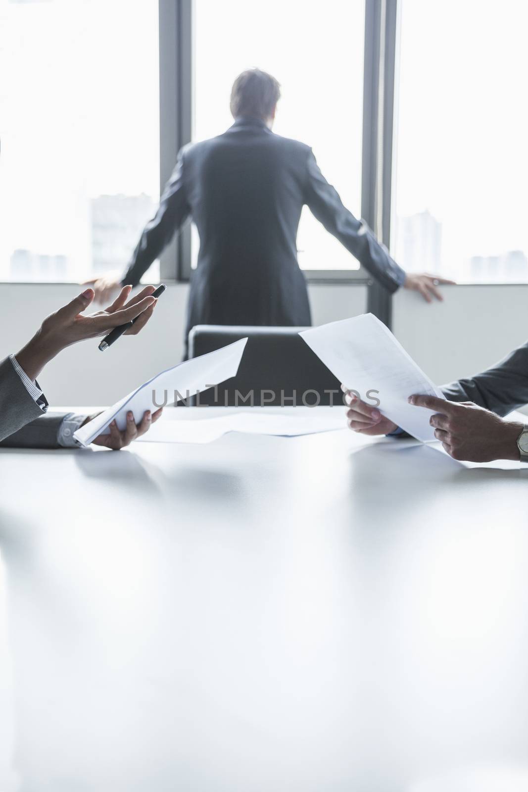Two business people discussing and gesturing over the table while another looks out the window, hands only