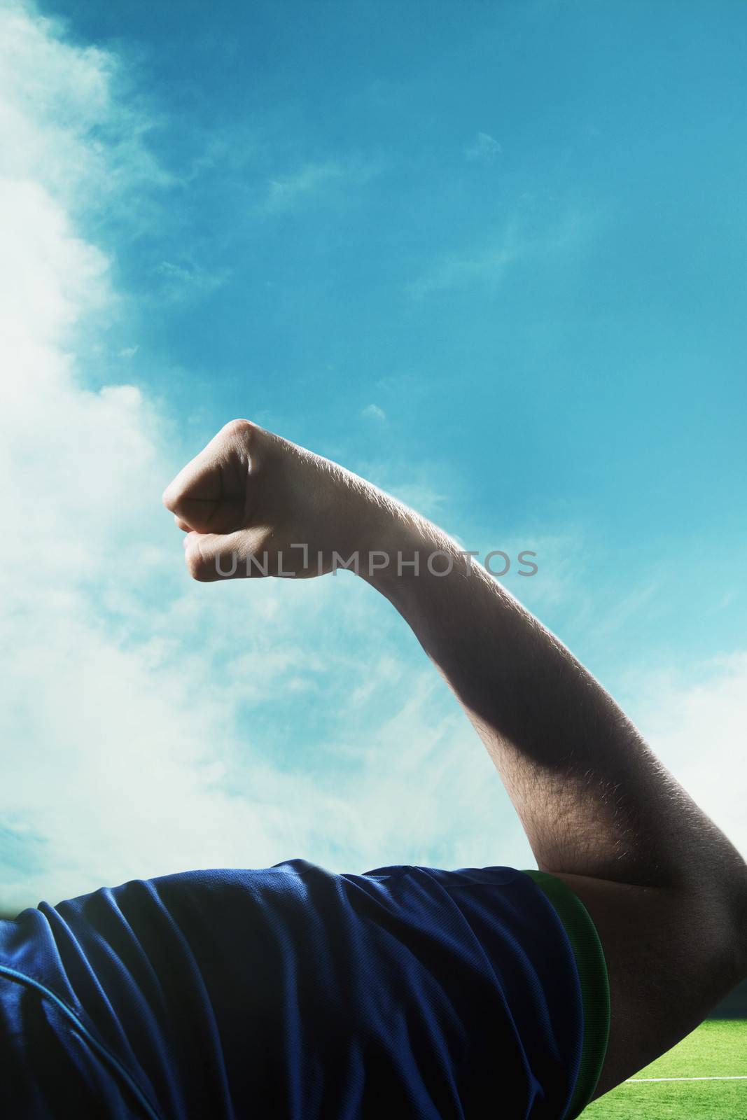 Soccer player flexing bicep during the day with sky in background