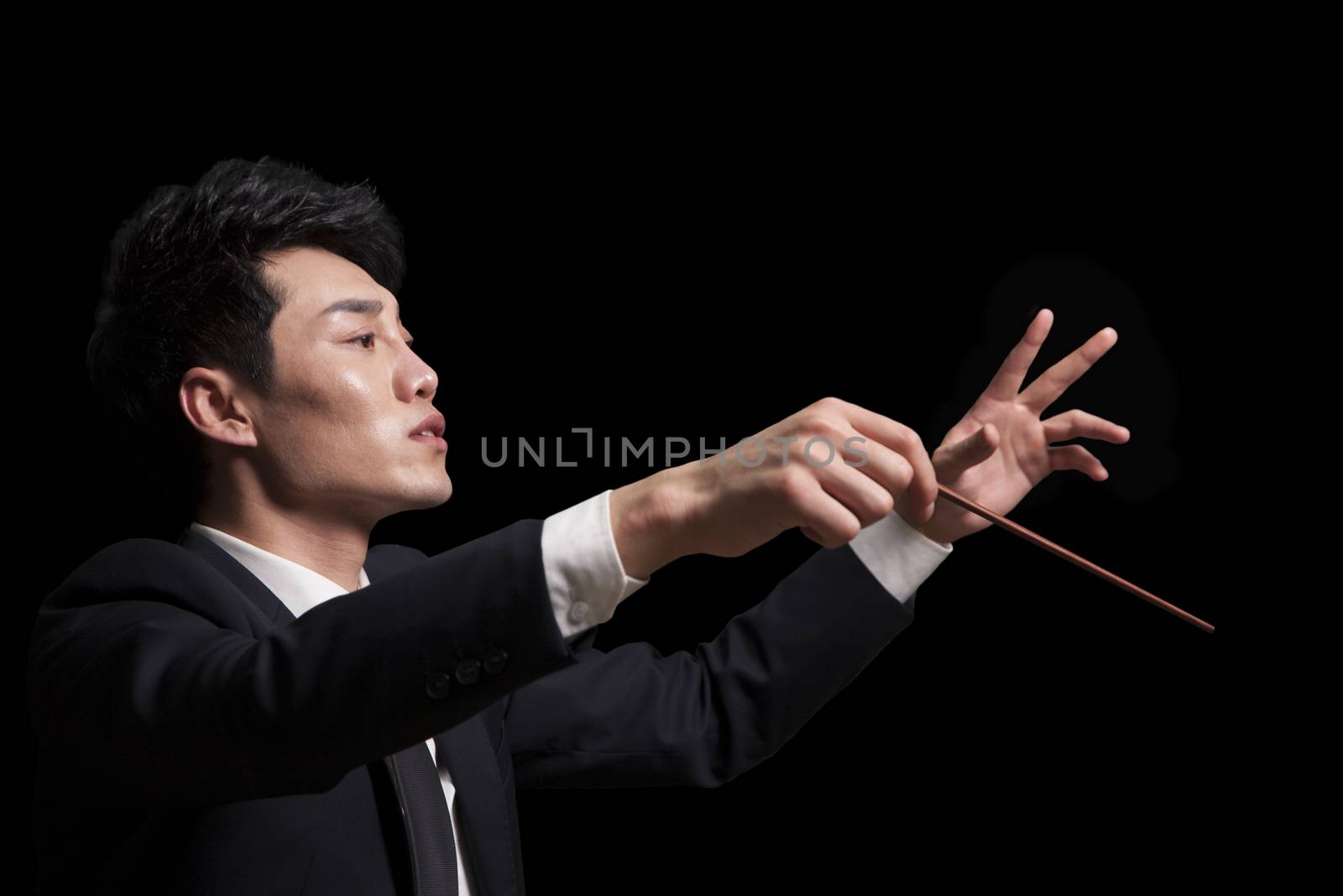 Young conductor with baton raised, black background