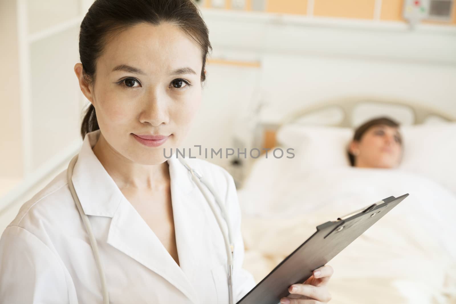 Portrait of smiling doctor holding a medical chart with patient lying in a hospital bed in the background