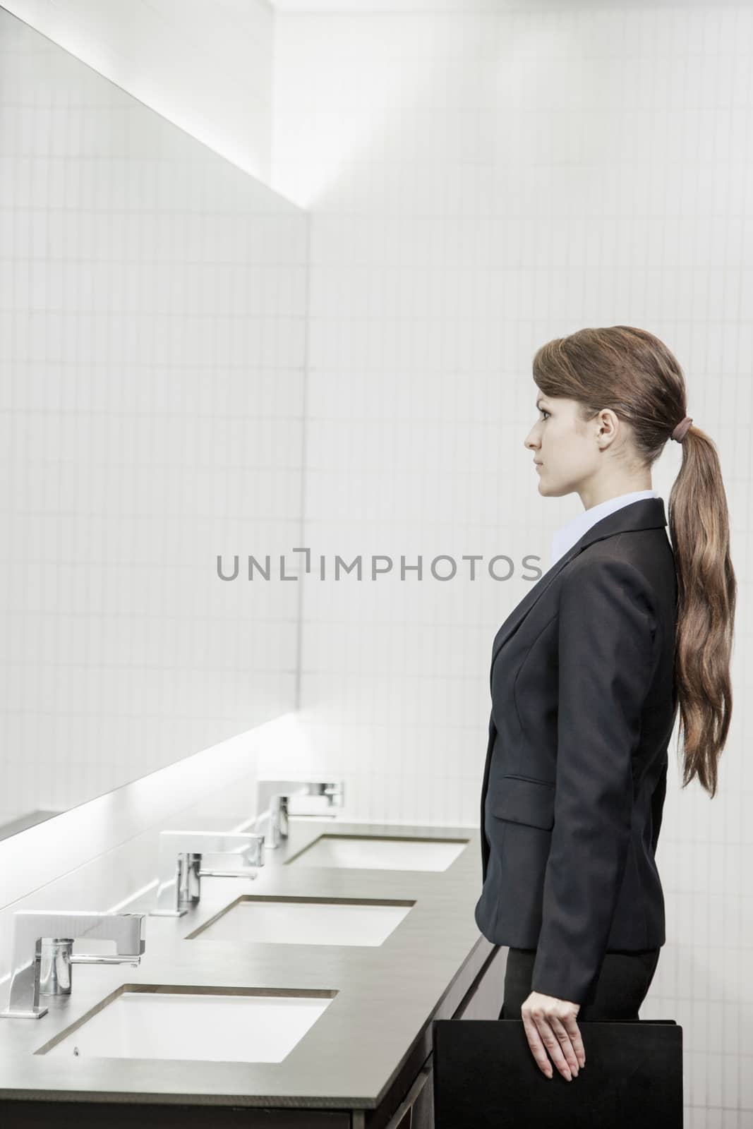 Young businesswoman with long hair looking into the mirror and preparing herself in the bathroom