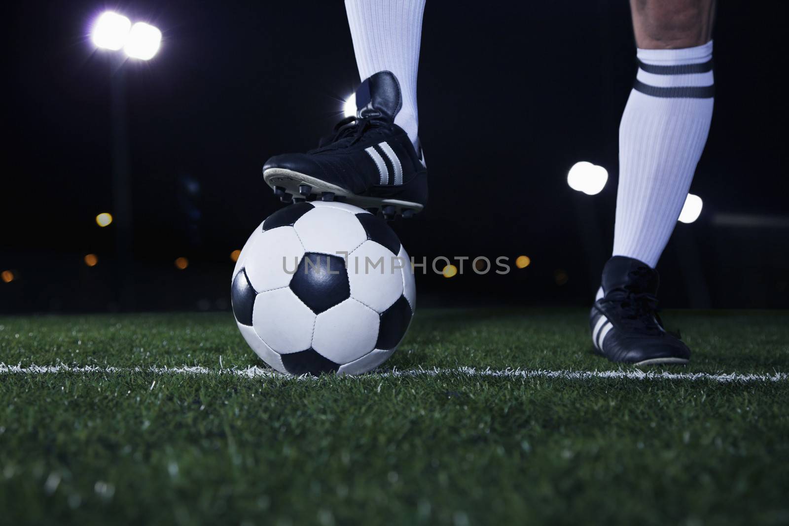 Close up of feet on top of soccer ball on the line, night time in the stadium by XiXinXing