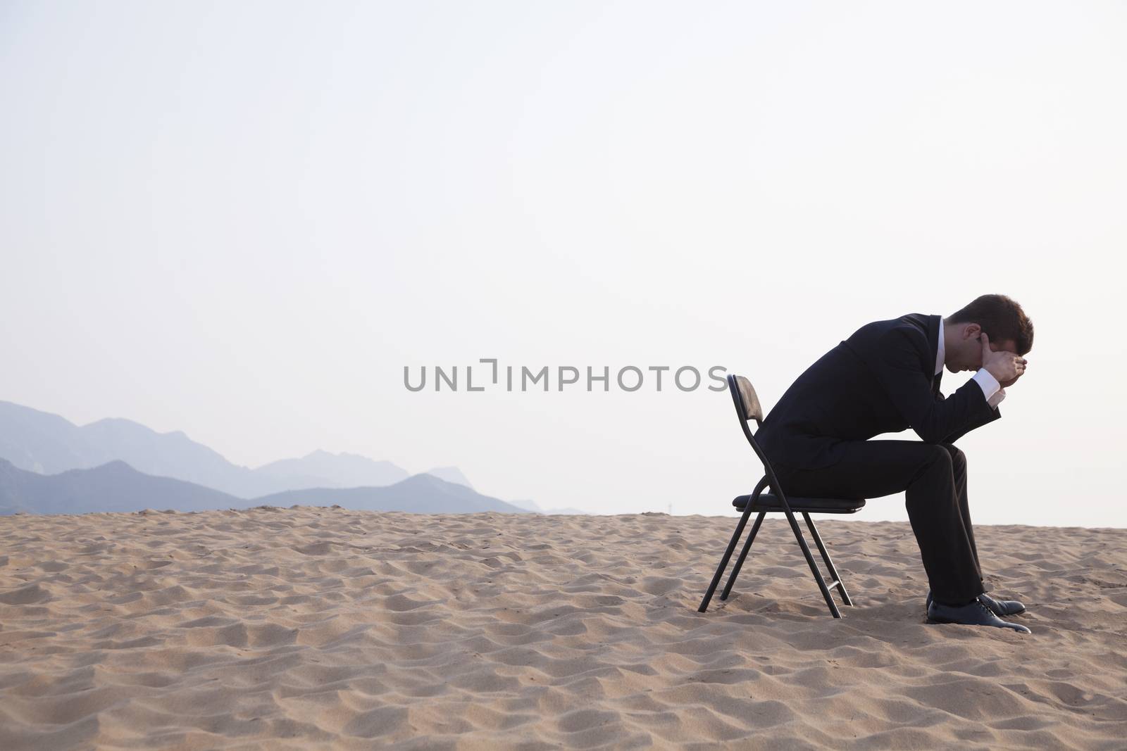 Businessman sitting with his head in his hands in the middle of the desert by XiXinXing