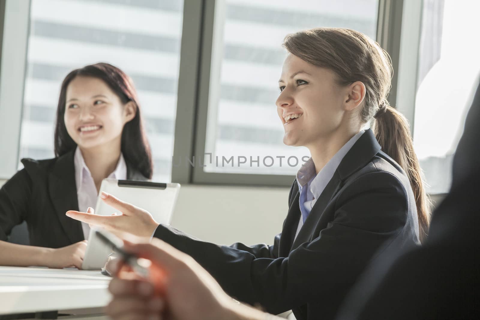 Two businesswomen smiling, discussing, and gesturing during a business meeting