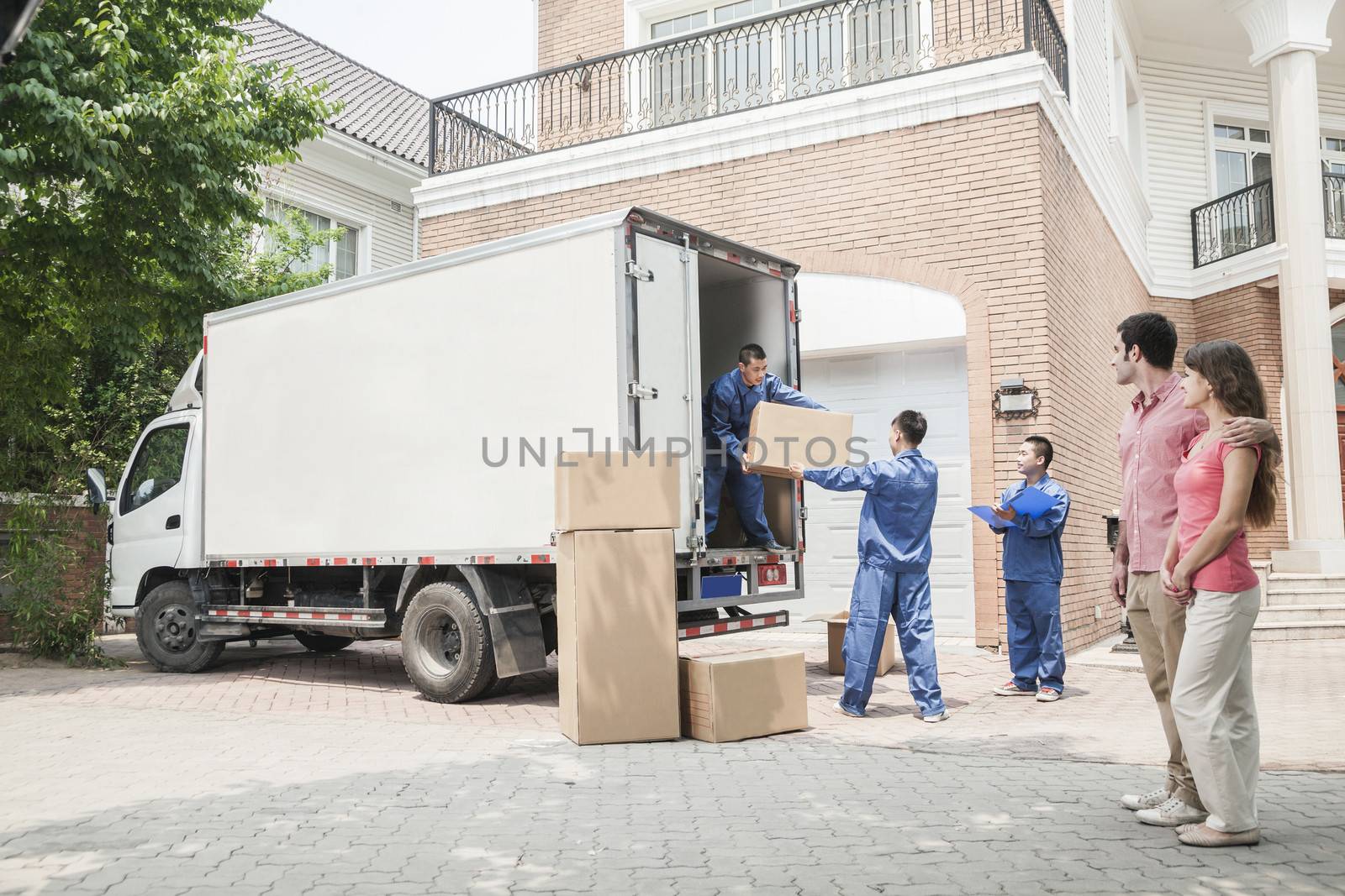 Young couple watching movers move boxes from the moving van by XiXinXing