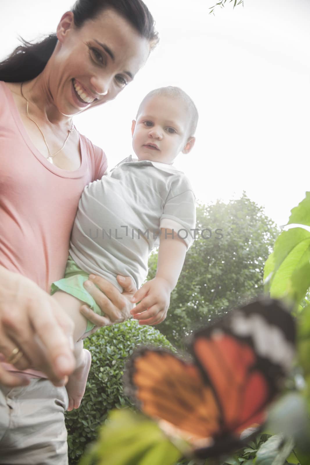 Smiling mother and son pointing and looking at a butterfly in the garden