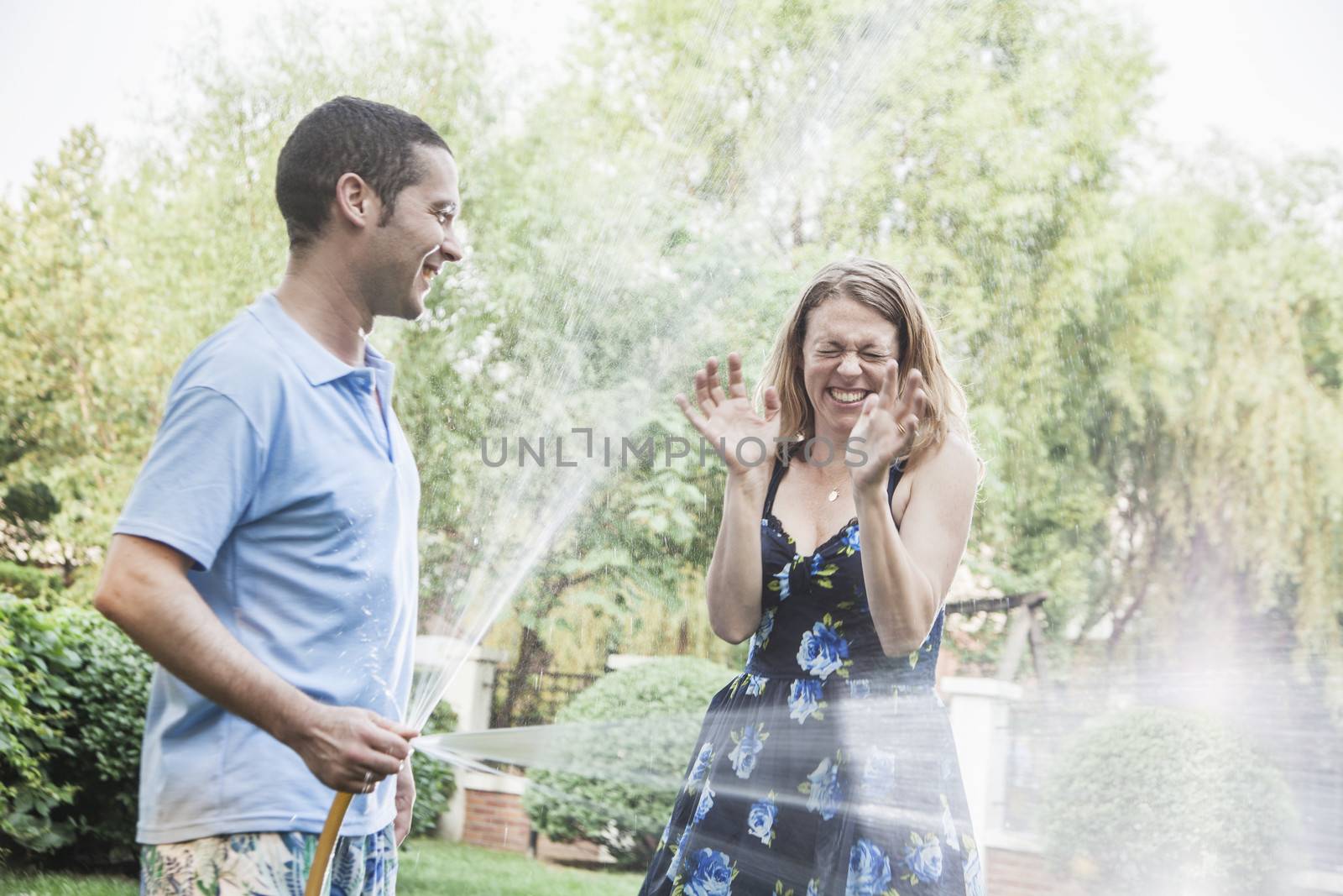 Couple playing with a garden hose and spraying each other outside in the garden 